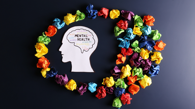 A piece of paper shaped like a person's head with the words mental health written in the middle with wadded up pieces of colored paper laying around the person's head.