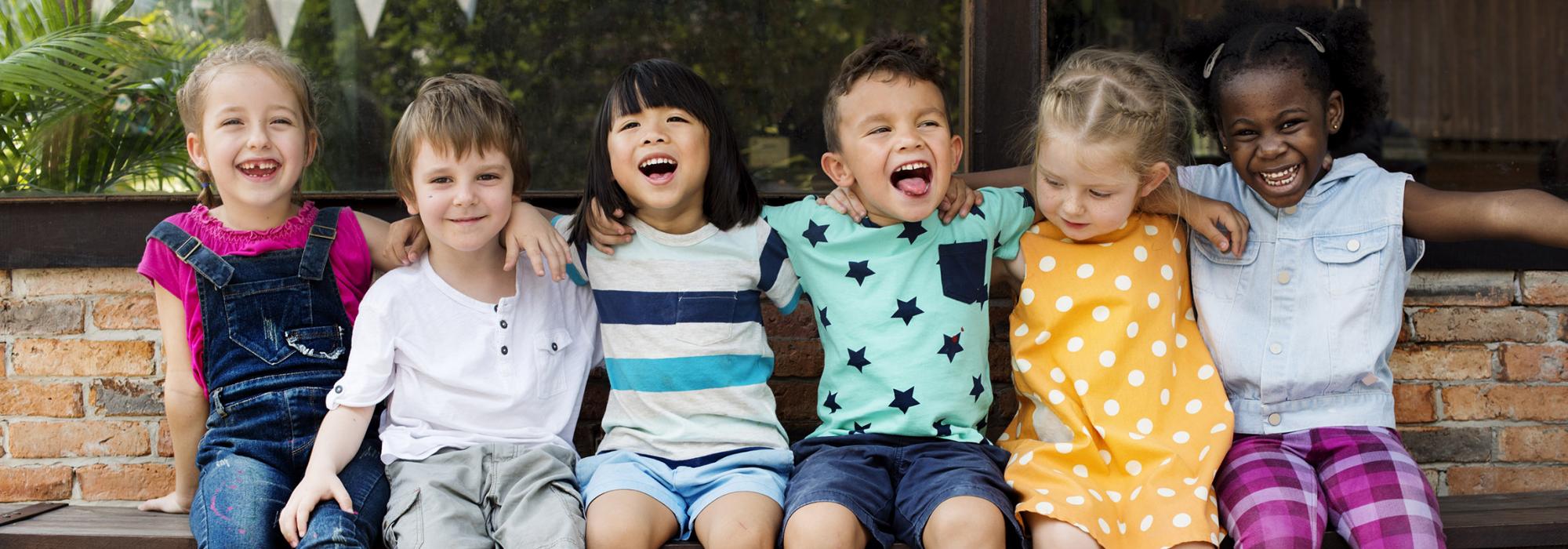 Image of six children sitting on a bench laughing